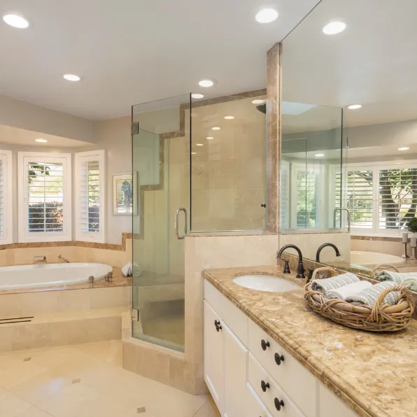 Bathroom remodeling project in Los Angeles with glass shower enclosure, bathtub, stone vanity countertop, tile flooring, and bright recessed lighting