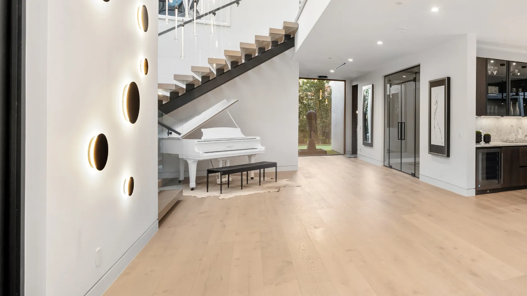 After interior remodeling project in Los Angeles with modern staircase, glass railing, light wood flooring, piano area, designer lighting, and refined open interior finishes