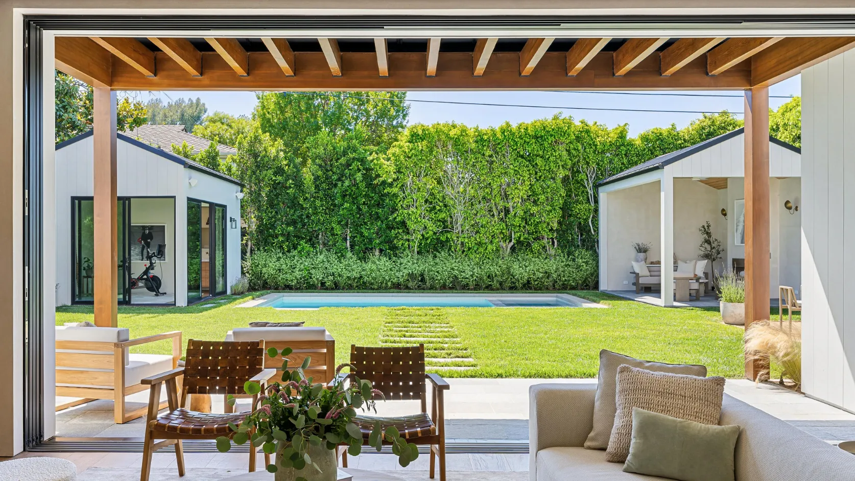 After outdoor living remodeling project in Los Angeles with modern backyard pool, covered patio, open indoor outdoor connection, lounge seating, and upgraded entertainment space