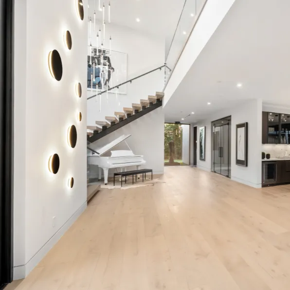 Interior remodeling project in Los Angeles with modern staircase, glass railing, piano area, light wood flooring, wall lighting, and open luxury interior design
